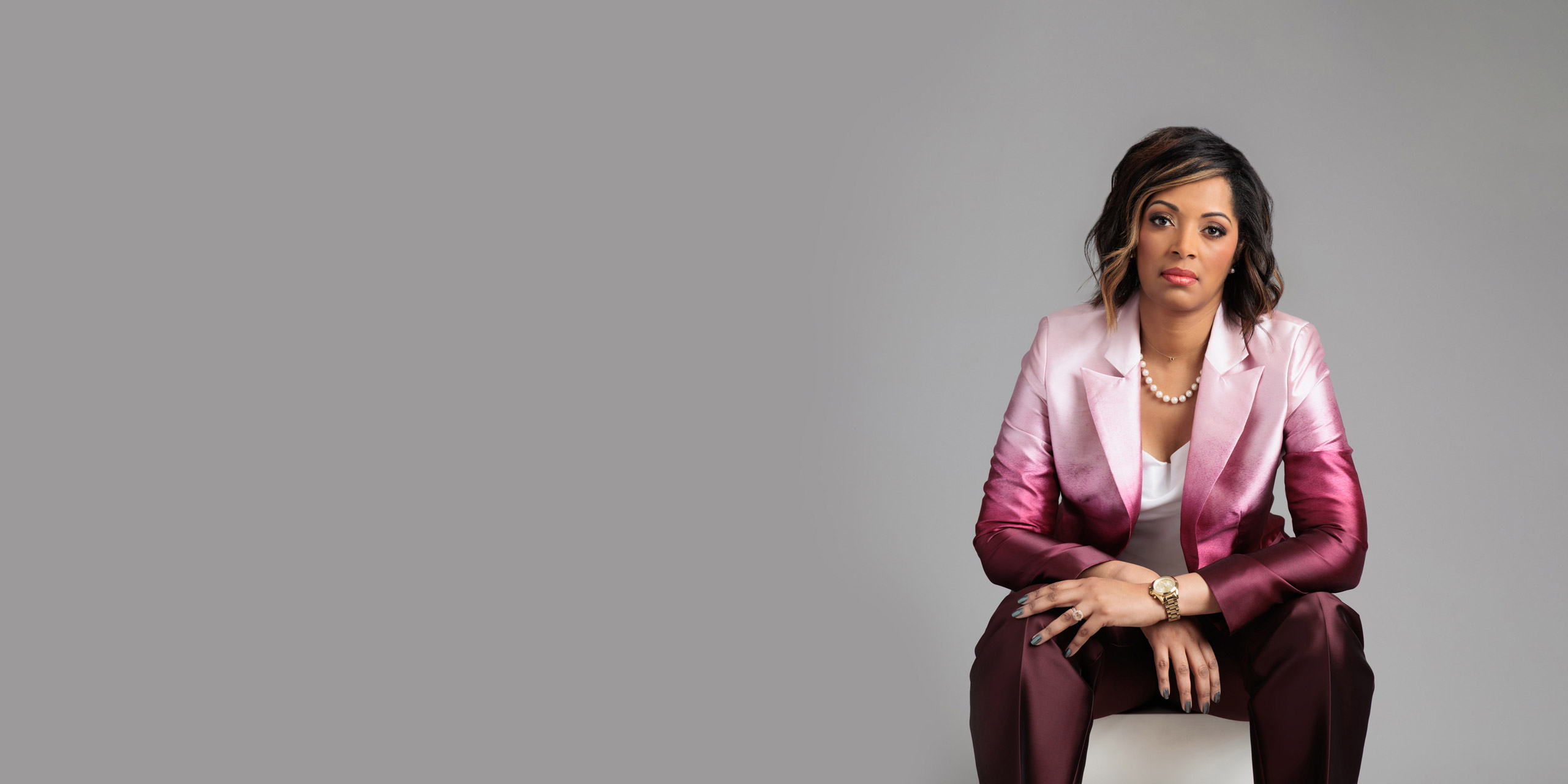 Kaye Monk-Morgan is seated, wearing a pink gradient suit.